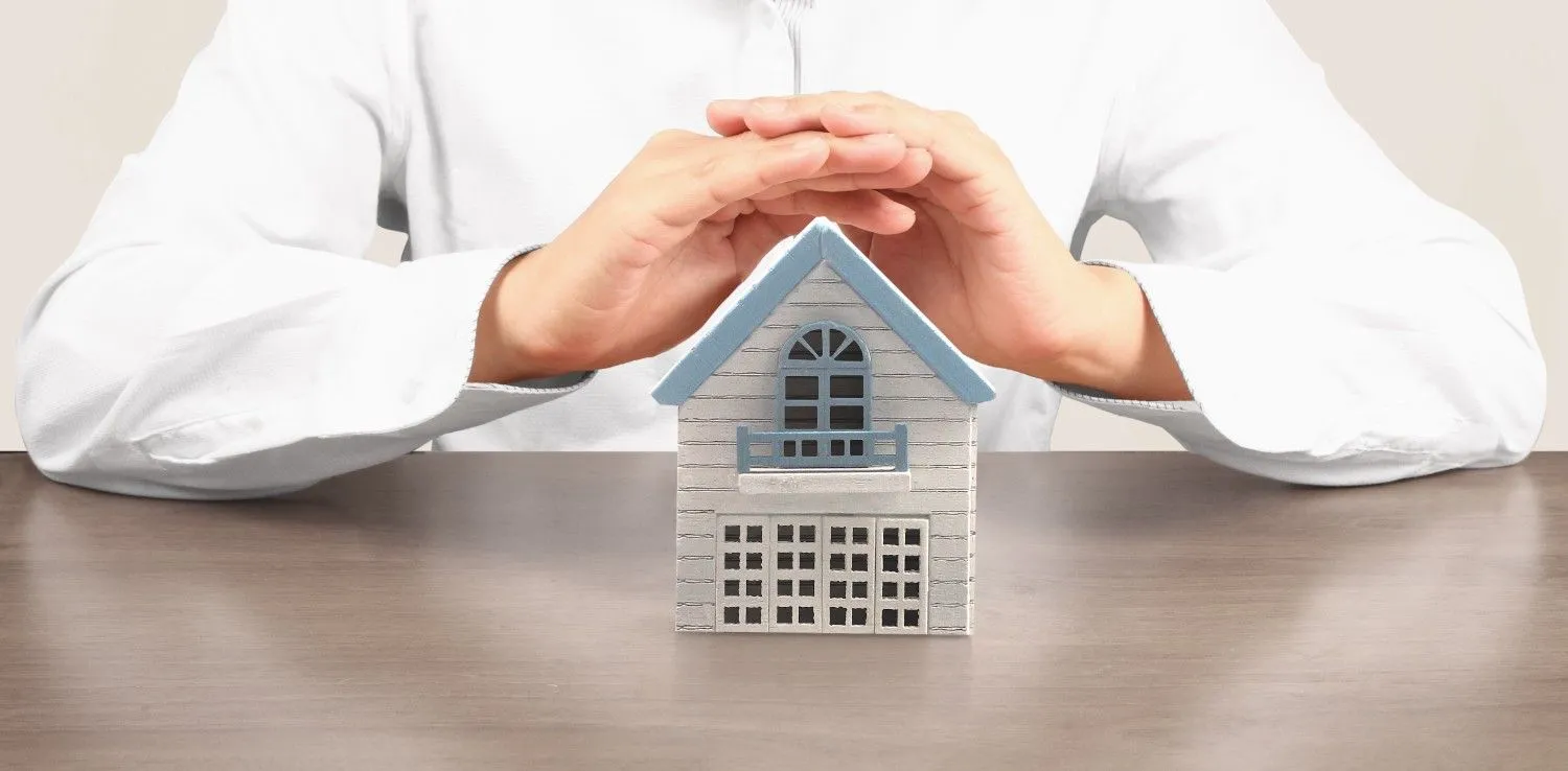 Hands sheltering a small house to show home insurance protection