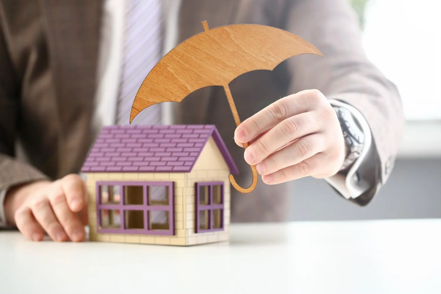 Umbrella held over a model house before damage happens